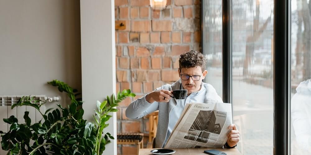 pessoa tomando café enquanto lê um jornal, aprendendo o que é um lide jornalístico
