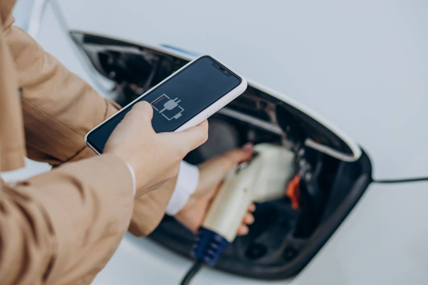 Mulher recarregando um dos veículos elétricos com o celular na mão acompanhando o nível da bateria do veículo