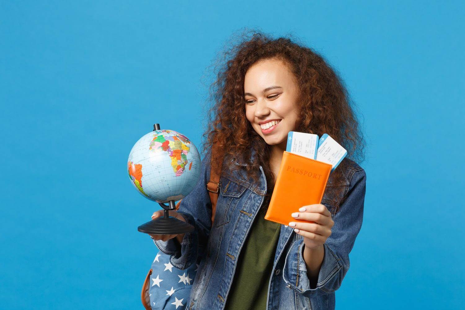 Mulher jovem intercambista segurando um globo, um passaporte e passagens depois de saber quais tipos de intercâmbio existem.