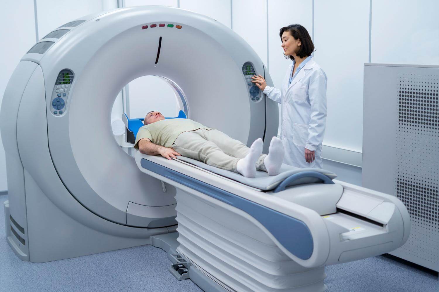 Homem deitado em equipamento de tomografia com a médica ao lado.