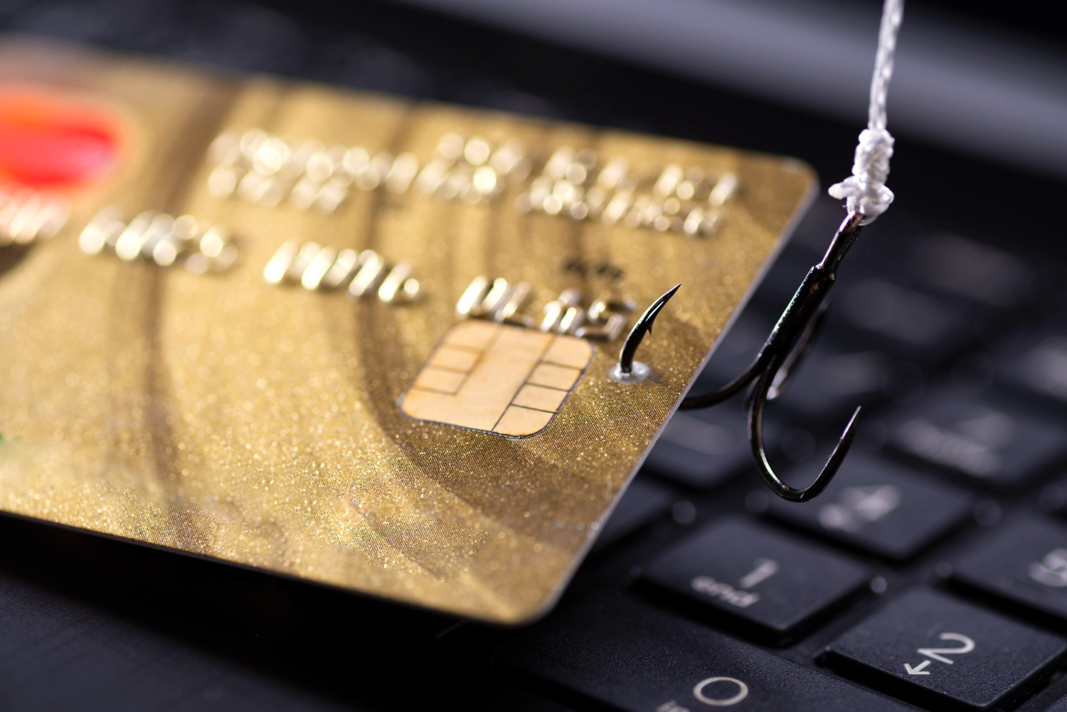 Imagem de cartão de crédito em anzol sobre teclado de computador representando golpe bancário pela internet.