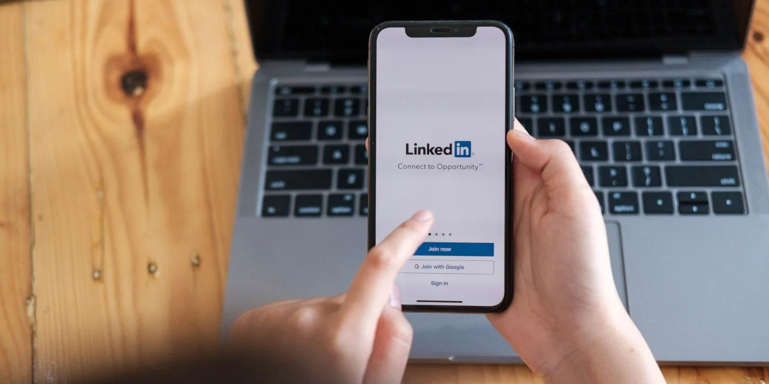 Mulher segura smartphone com aplicativo do LinkedIn na tela, enquanto aprende a como usar o LinkedIn