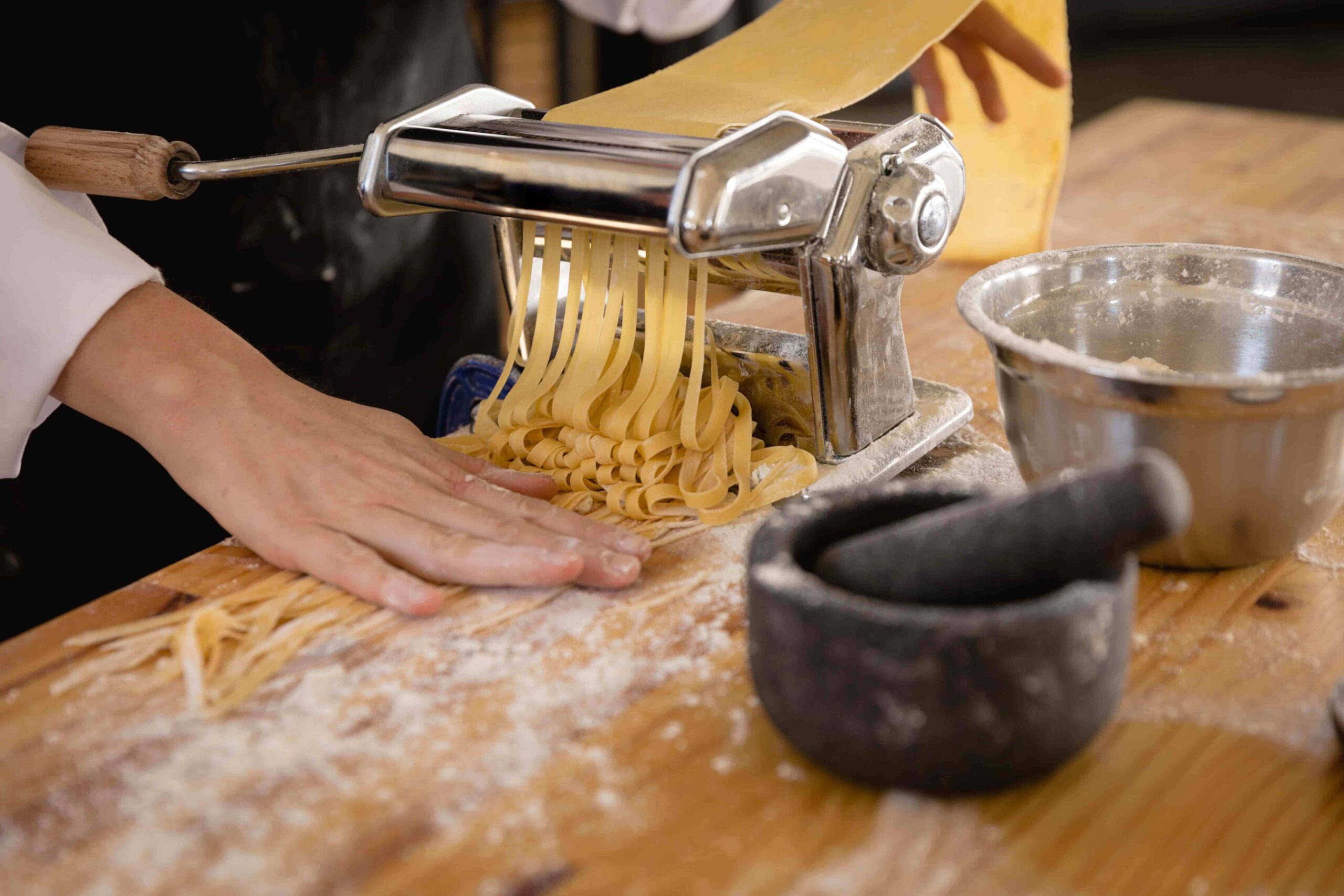 Imagem de um cozinheiro utilizando equipamentos para fazer massas durante preparo de macarrão.